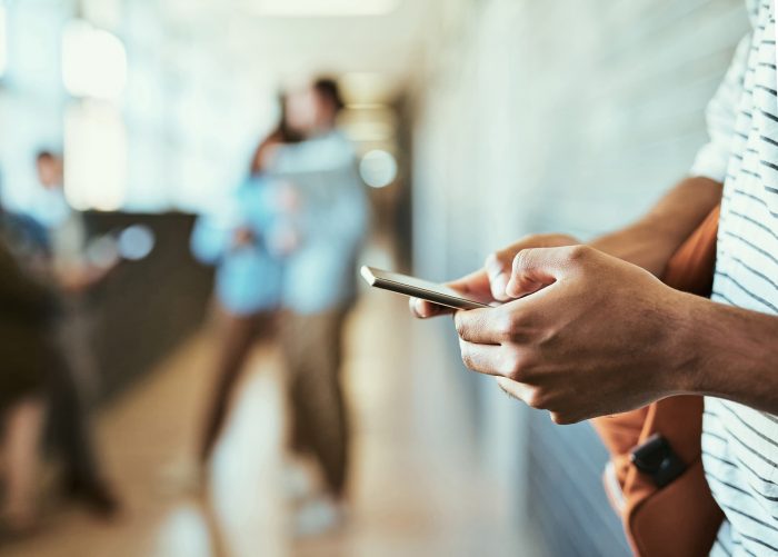 A man standing in a hallway typing on his mobile phone